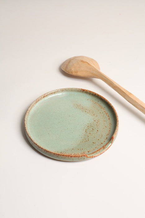 Ceramic spoon rest in a green satin glaze, with a carved spoon next to it, on a white surface 