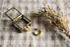 A pair of small gold hoop earrings, with a brass and glass jewellery box and dried flowers, on a neutral gingham surface