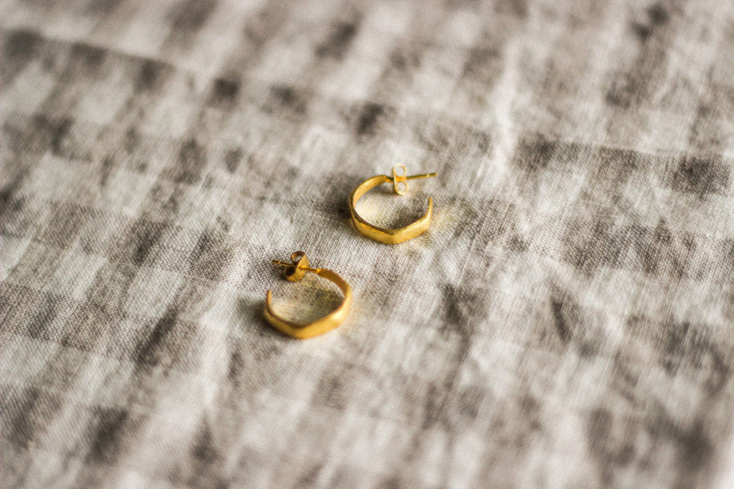 A pair of small gold hoop earrings on a neuutral gingham surface