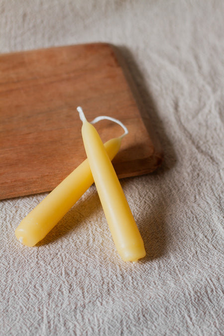 Two beeswax candles on a wooden cutting board with a linen surface background