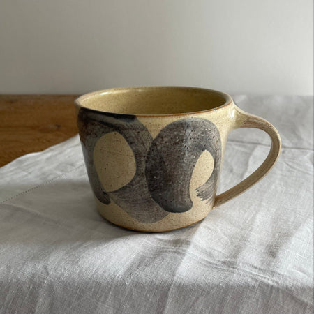 Stoneware mug in a beige glaze with a blue striped design, on a wooden table with a white cotton runner 