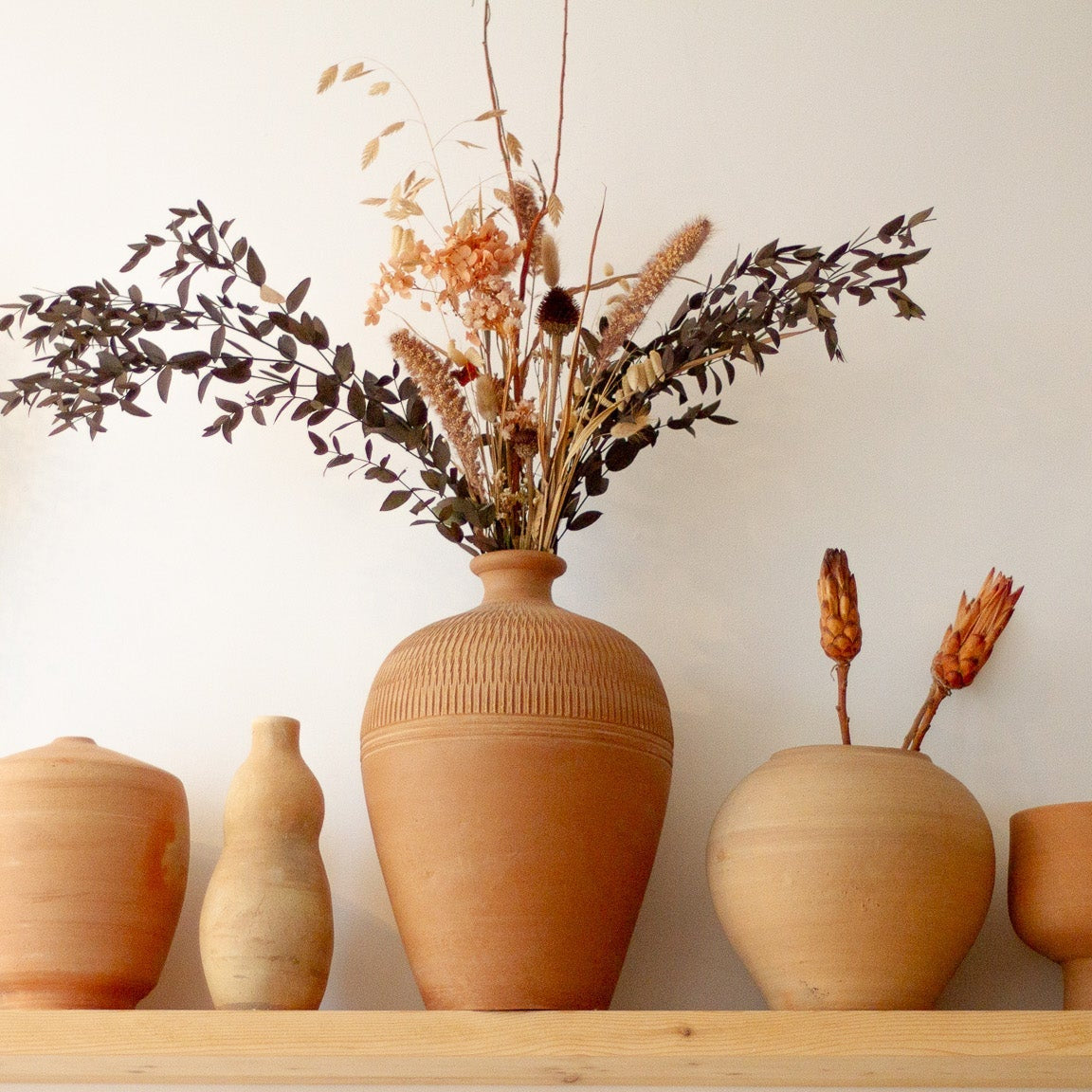 wooden shelf filled with terracotta pots and dried flowers 