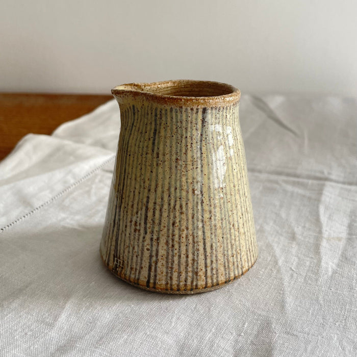 Beige stoneware milk jug with a blue striped design on a wooden table with a white cotton runner 