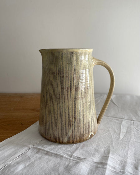Stoneware jug with a blue striped design, on a wooden table with a white cotton runner 