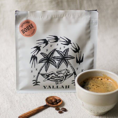 Coffee bag with palm tree design, coffee beans in a wooden coffee scoop, and cup of coffee on a linen surface